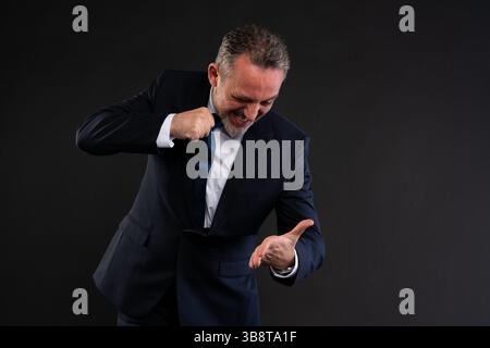 Businessman in suit pulling his tie with a clenched fist, expressing frustration or anger while looking down at his open palm. Concept of workplace st Stock Photo