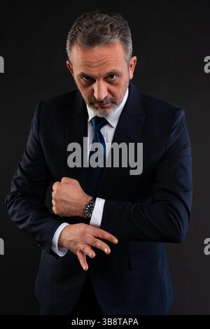 Mature businessman in a navy suit adjusting his shirt sleeve, looking seriously at the camera. Concept of confidence, elegance and professionalism. Stock Photo