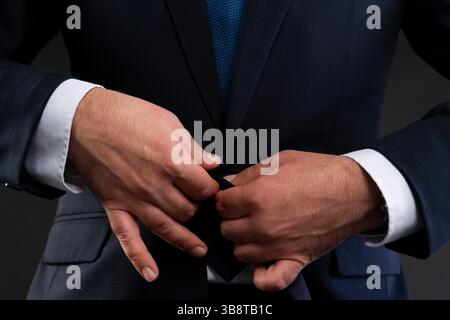Close-up of a man's hands buttoning his dark suit jacket, showcasing elegance and attention to detail in professional attire. Stock Photo