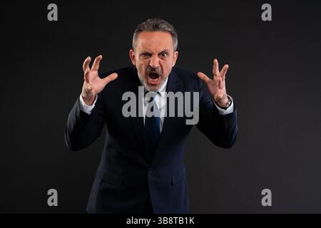 Furious businessman in formal suit screaming with hands up, expressing frustration, anger or stress. Studio shot on dark background Stock Photo