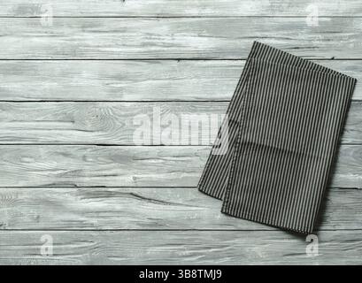 Gray wooden table with balck and white dark linen kitchen towel or textile napkin flat lay. Dark tablecloth on old gray wood tabletop. Copy space for Stock Photo