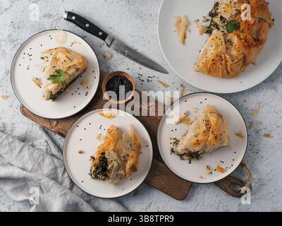 Greek pie spanakopita on gray background. Ideas and recipes for vegetarian or vegan Spanakopita Spinach Pie from fillo pastry. Slices pie on plates. C Stock Photo