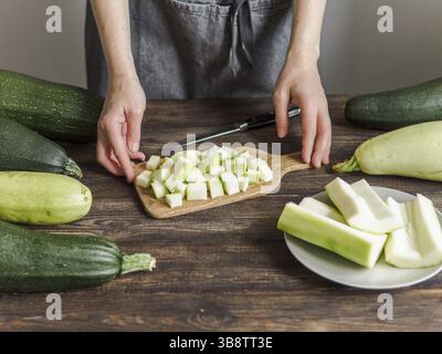 Zucchini harvest. Woman slices zucchini cubes for freezing on wooden table. Farm organic zucchini harvesting Stock Photo