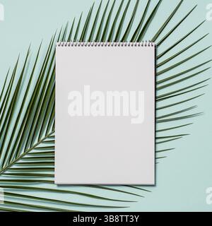 Blank paper notebook with pencil. Empty paper sketchbook with pencil and tropical leaf on blue background. Top view or flat lay. Copy space for text o Stock Photo