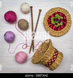 From above the colored balls of yarn in wicker basket with needles on white wooden board in Ukraine Stock Photo