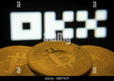 Dhaka, Bangladesh- 04 April 2025: Close-up of Bitcoin coins with the OKX logo visible on a screen in the background Stock Photo