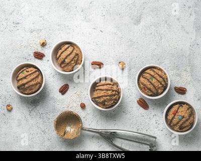 Safe-to-eat raw monster cookie dough in small portion bowl, ice cream scoop and nuts on gray cement background. Ideas and recipes for kids and toddler Stock Photo