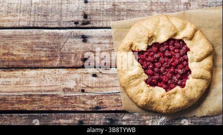 Perfect raspberry galette. Delicious rustic homemade tart with frozen or fresh raspberries on old wooden background. Beautiful round shape galette wit Stock Photo