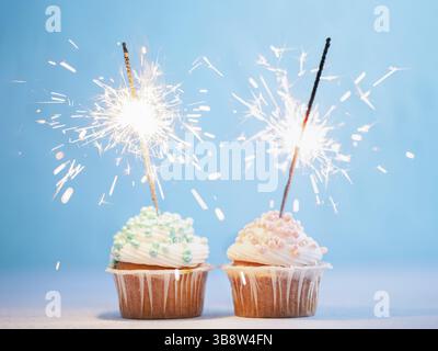 Two cupcakes decorated with colorful sprinkles and sparklers. Festive cupcakes with blue and pink sprinkles on blue background Stock Photo