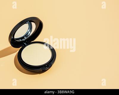 Compact powder on yellow or cream background. Female pressed powder in ajar opened black plastic case with mirror, copy space for text or design. Hard Stock Photo