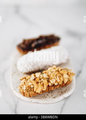 Set of three homemade eclairs on marble background. Close up view of delicious healthy profitroles with different decor elements - chocolate, peanut a Stock Photo