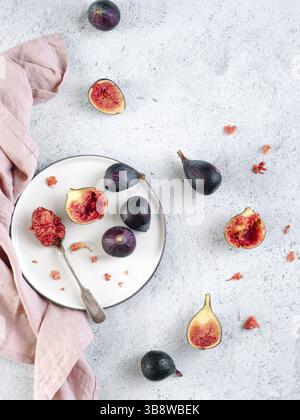 Half and whole figs on gray cement or stone background. Ripe violet figs with copy space for text. Figs flesh in teaspoon on plate and figs on tableto Stock Photo