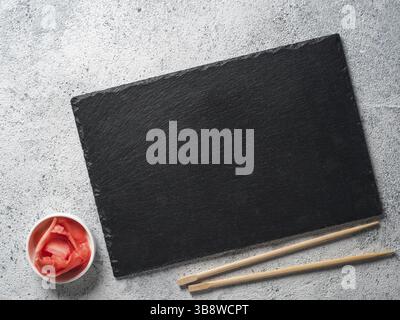 Empty slate plate on gray cement background with chopsticks and pickled ginger. Copy space. Top view or flat-lay. Concept for restaurant and delivery Stock Photo