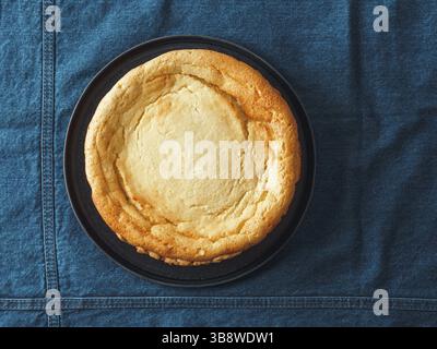 Plate with whole cheesecake pie on table with jeans tablecloth. Classic cheesecake flat lay or top view. Vertical Stock Photo