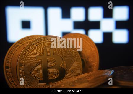 Dhaka, Bangladesh- 04 April 2025: Close-up of Bitcoin coins with the OKX logo visible on a screen in the background Stock Photo