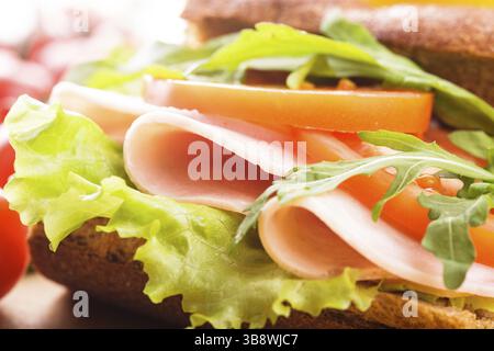 Wholegrain sandwich with ham, tomato, lattuce and arugula with glass of orange juice. Breakfast Stock Photo