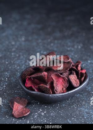 Baked beet slices. Healthy homemade beetroot chips in plate on dark blue background. Copy space Stock Photo