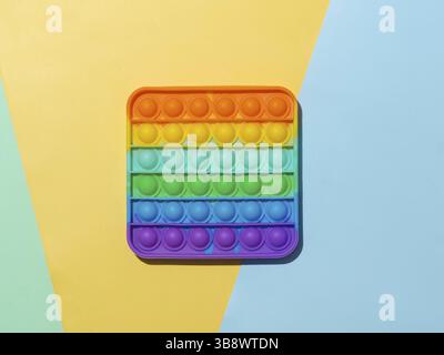Popit on multicolor background with copy space. Popular silicone colorful antistress pop it toy for child on asure, yellow and blue paper background. Stock Photo