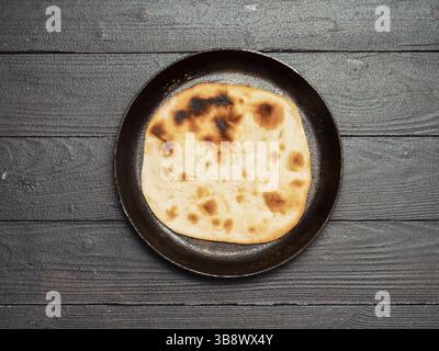 Fresh naan bread in cast-iron pan on dark wooden background with copy space. Top view of perfect naan flatbread black circle cast iron pan Stock Photo