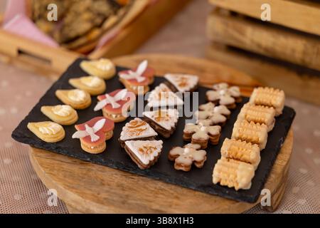 Various christmas cookies with different shapes and icings are displayed on a black slate plate, ready to be enjoyed Stock Photo