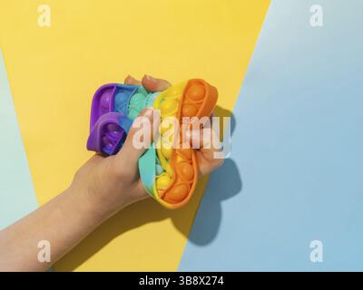 Female hand with popit toy clenched into fist, top view over two-shadows blue background. Popit on blue background with copy space. Popular silicone c Stock Photo