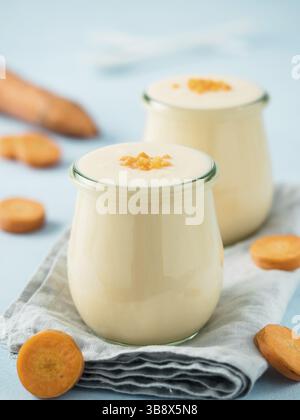 Yogurt with carrot. Vegetable yogurt. Two glass jar with yellow orange yoghurt or milkshake and fresh carrot on blue background. Copy space for text. Stock Photo