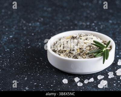 Sea salt scented herb rosemary and lemon zest. Sea salt with aromatic herbin small bowl on dark blue background. Scented salt and ingerdients. Copy sp Stock Photo