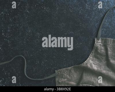 Cooking and kitchen background - trendy denim cotton apron on dark background with copy space. Gray kitchen apron on dark table as kitchen background Stock Photo