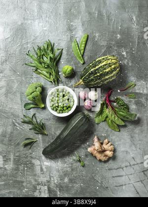 Green vegetables and herbs on gray background, top view.Still life with green peas, zucchini, bean-pod, pumpkin, ginger, garlic, broccoli, tarragon, b Stock Photo