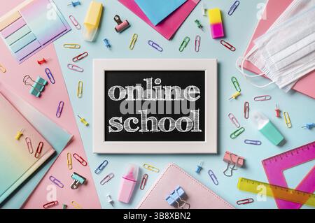 Black chalkboard with letters online school. School supplies, pencils, scissors and colored books on blue and pink background. Top view or flat lay. E Stock Photo