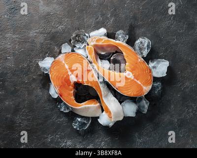 Two raw wild salmon steaks on ice over black textured background. Salmon steaks top view or flat lay Stock Photo
