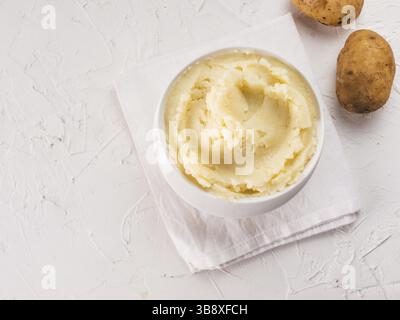 Mashed potatoes in white bowl with cloth napkin on textured concrete white background. Top view or flat lay. Copy space Stock Photo