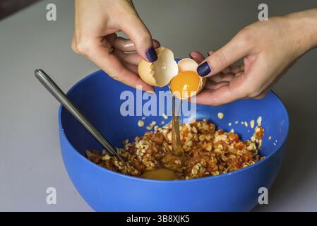 Hand pours out raw egg of the shell in blue bowl Stock Photo