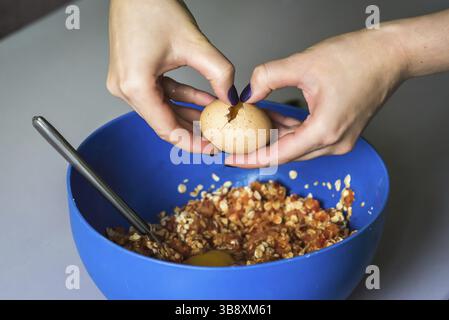 Hand pours out raw egg of the shell in blue bowl Stock Photo