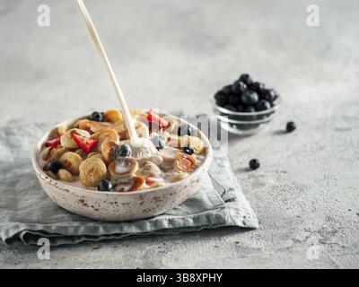 Trendy food - pancake cereal. Milk pouring on heap of mini cereal pancakes in bowl. Tiny cereal pancakes with berries in craft plate over gray cement Stock Photo