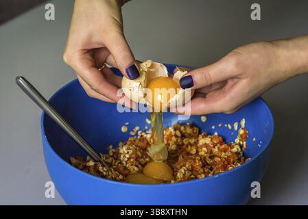 Hand pours out raw egg of the shell in blue bowl Stock Photo