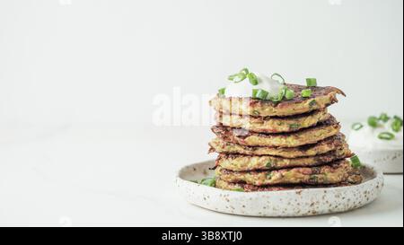 Zucchini fritters. Traditional zucchini fritters in stack on white background. Zucchini pancakes or fritters with green onion and parmesan cheese, ser Stock Photo