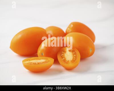 Orange tomatoes on white marble table. Yellow or orange tomatoes heap with two half sliced tomato. Copy space for text Stock Photo
