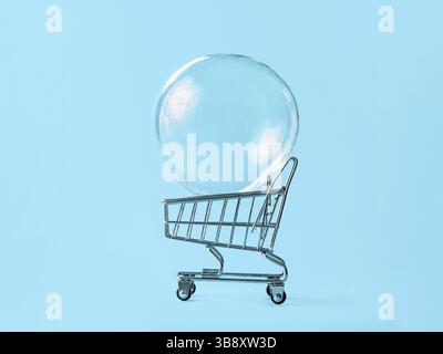 Shopping cart with soap bubble on bright blue background. Ephemeral happiness from shopping, economic bubble, financial crisis concept. minimalist cre Stock Photo