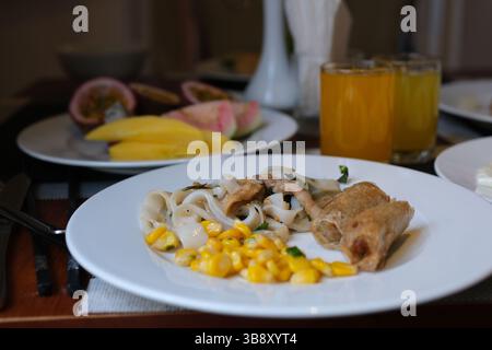 on a white plate lunch dinner corn rice vermicelli with soy meat and two fried spring rolls mango and passion fruit juice as well as fruits for breakfast at the hotel buffet. High quality photo Stock Photo