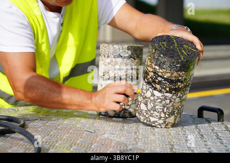 Worker Using Colored Chalk to Mark and Place Number on Cylindrical Core Sample from Asphalt Road Stock Photo