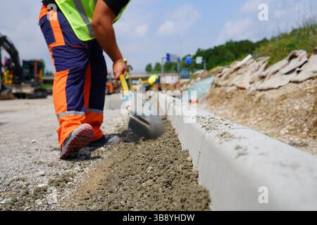 Worker Using Shovel to Place Concrete Along Road Curb on Construction Site Stock Photo