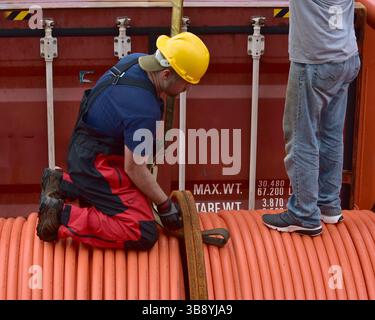 Crane unloads rolls of PVC cable sheathing from cargo ship. Crane is ...