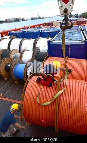 Crane unloads rolls of PVC cable sheathing from cargo ship. Worker ...