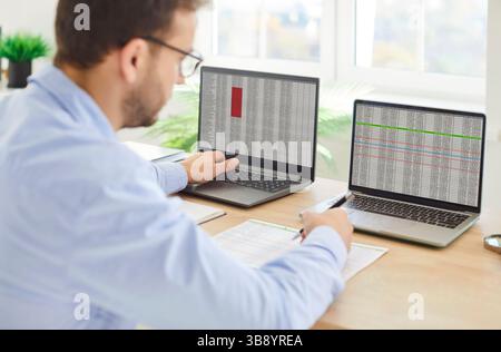 Young focused serious business man working on laptop in office analyzing company finances Stock Photo