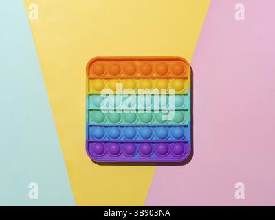 Popit on multicolor background with copy space. Popular silicone colorful antistress pop it toy for child on blue, yellow and pink paper background. T Stock Photo