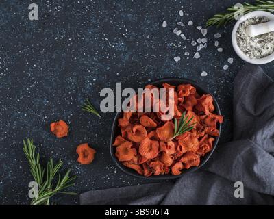 Baked carrot slices with coarse sea salt scented rosemary. Vegan diet food idea and recipe. Healthy homemade carrot chips in plate and ingredients on Stock Photo