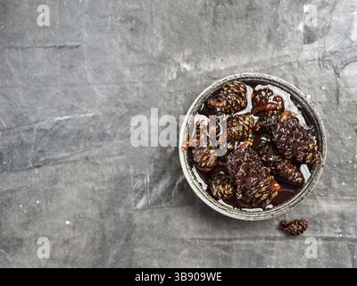 Delicious jam with baby pine cones in small bowl. Traditional Siberian dessert - young pine cones jam on gray textured background. Top view or flat la Stock Photo