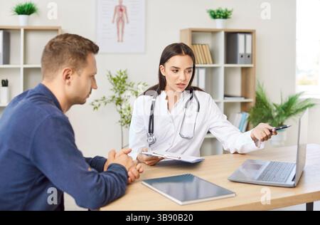 Female Doctor Or Nurse Consulting Male Patient Using Laptop In Hospital Office Stock Photo