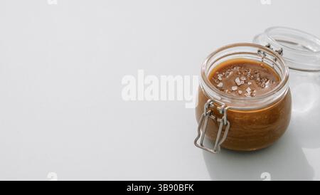 Salted caramel in glass jars on light neutral background. Brown caramel or condensed milk with sea salt crystalls. Long horizontal banner, copy space Stock Photo
